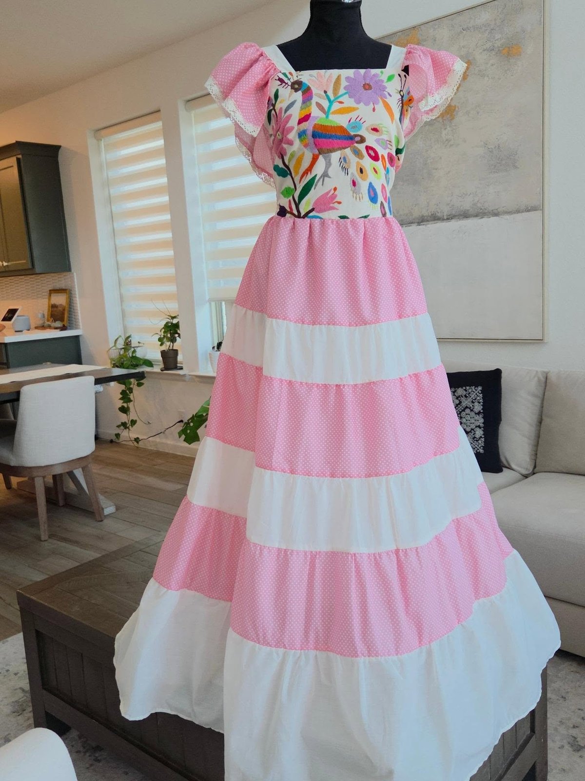 Colorful childrens dress on mannequin with floral print bodice, ruffled off-shoulder sleeves, and alternating pink and white striped tiered skirt