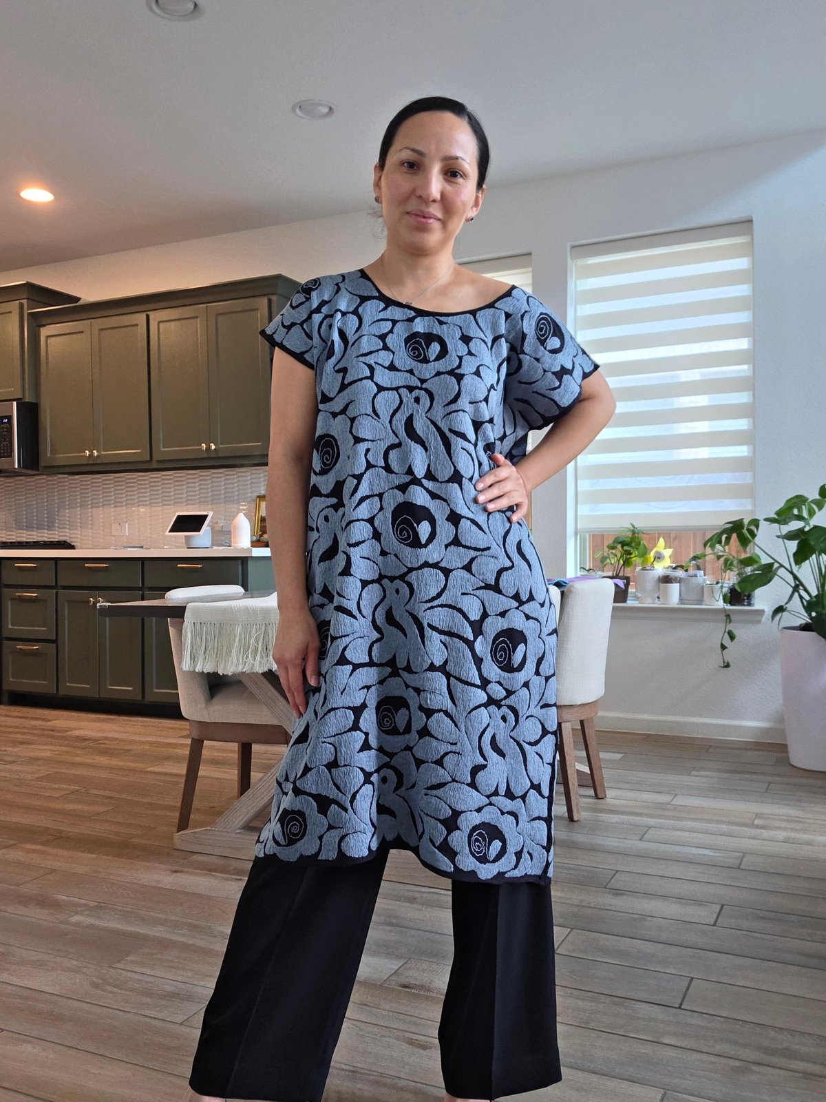 Mujer con huipil azul de manga corta con flores negras y pantalón negro en cocina moderna